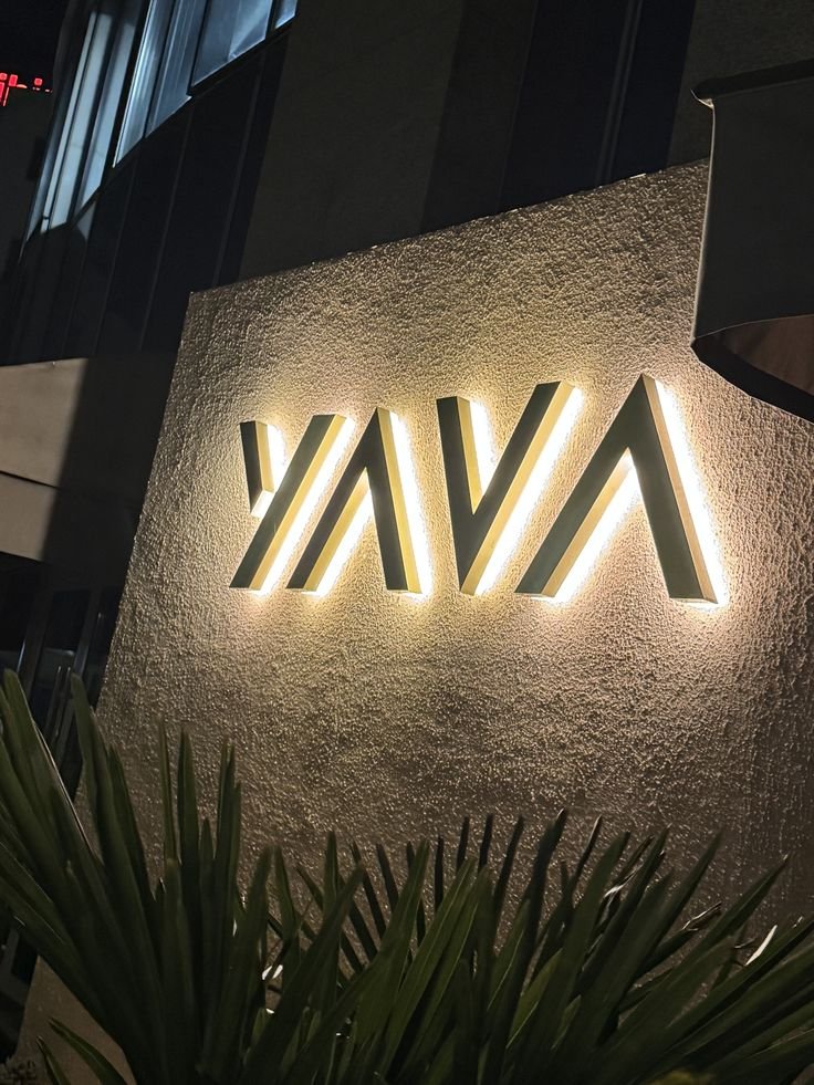 Logotipo de Yava iluminado con letras plateadas sobre pared clara
